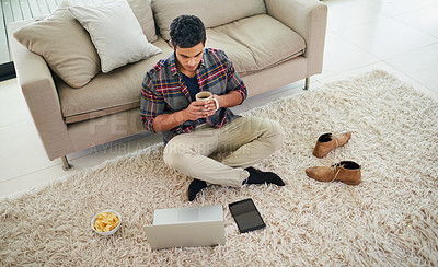 Buy stock photo Shot of a handsome young man using his laptop while relaxing on the floor at home