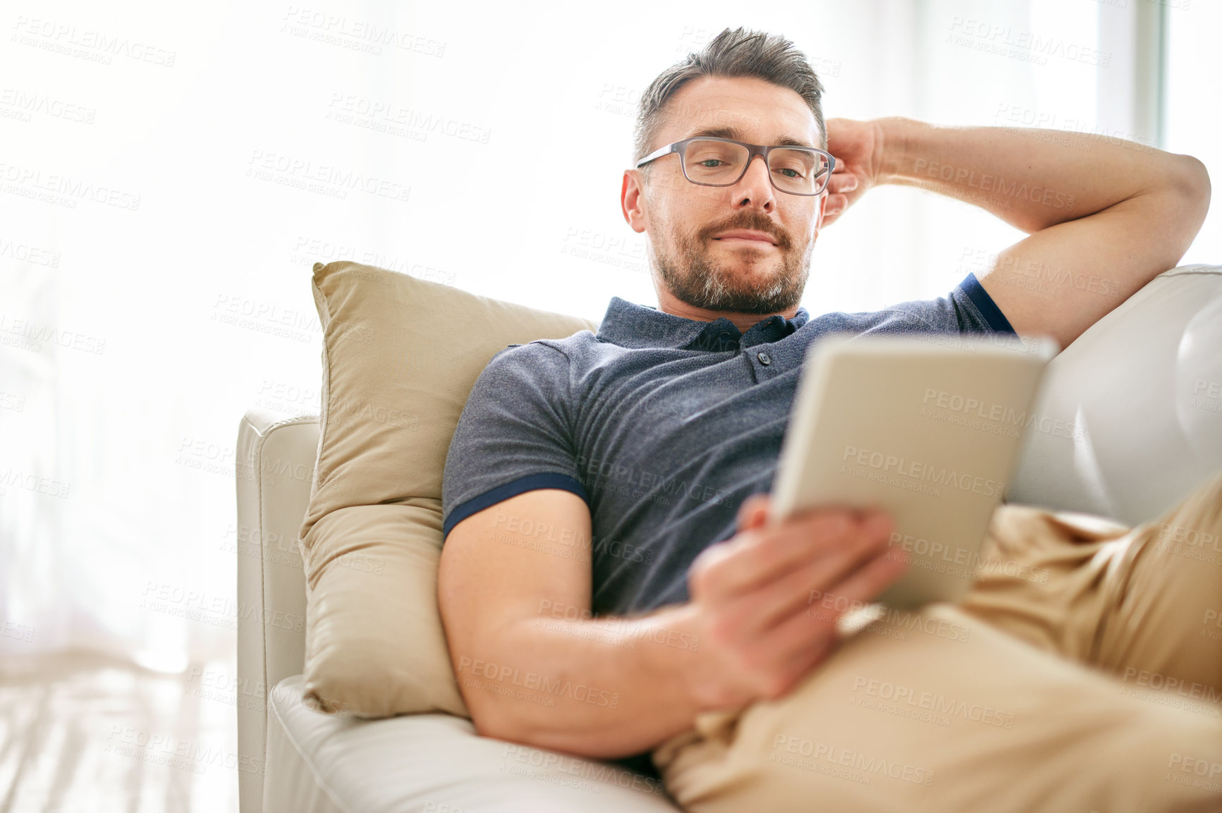 Buy stock photo Tablet, relax and man on a sofa in the living room watching a video on social media or the internet. Rest, browsing and mature male person reading an online blog on digital technology at his home.