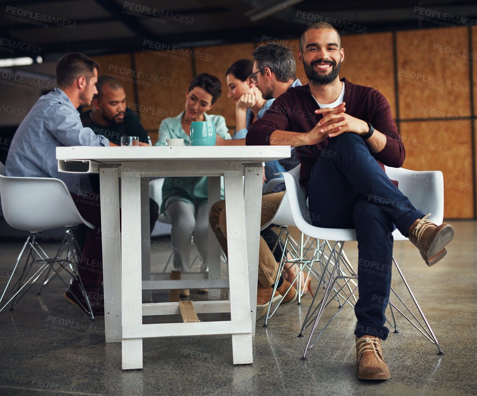 Buy stock photo Portrait of a young man sitting at a table in an office with colleagues working in the background