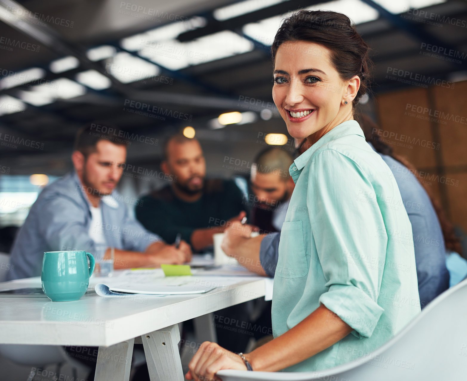 Buy stock photo Portrait of a young woman sitting at a table in an office with colleagues working in the background