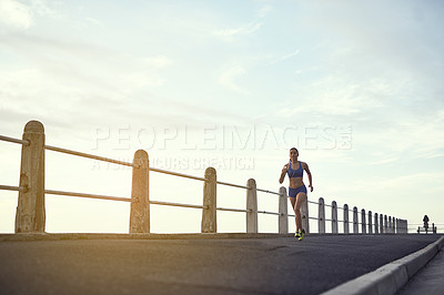 Buy stock photo Shot of a fit young woman out for a run on the promenade