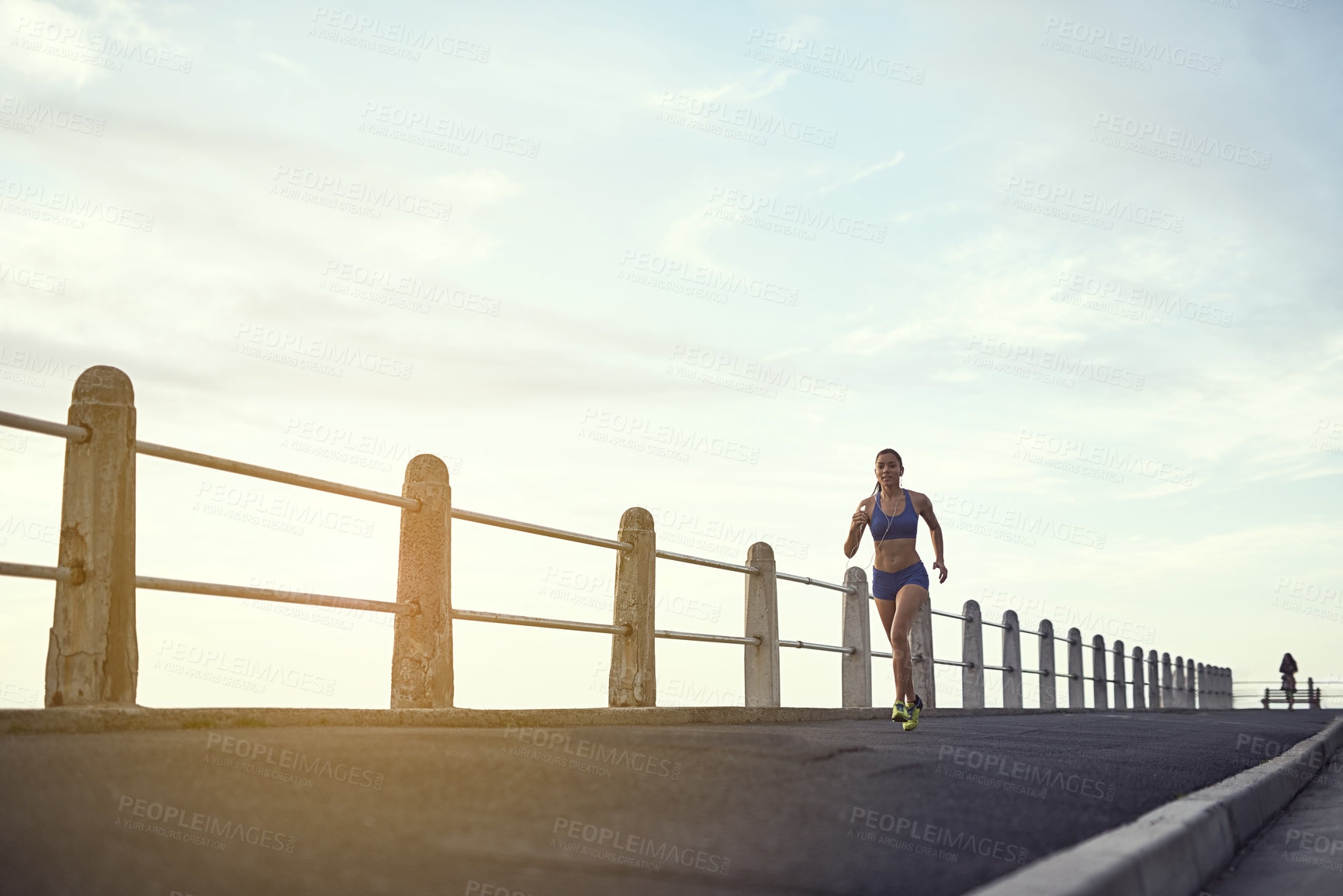 Buy stock photo Shot of a fit young woman out for a run on the promenade