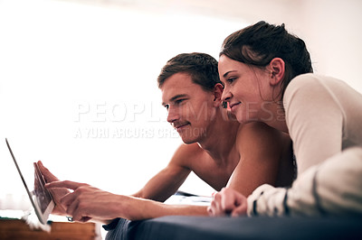 Buy stock photo Shot of a young couple spending a lazy day in bed with their tablet