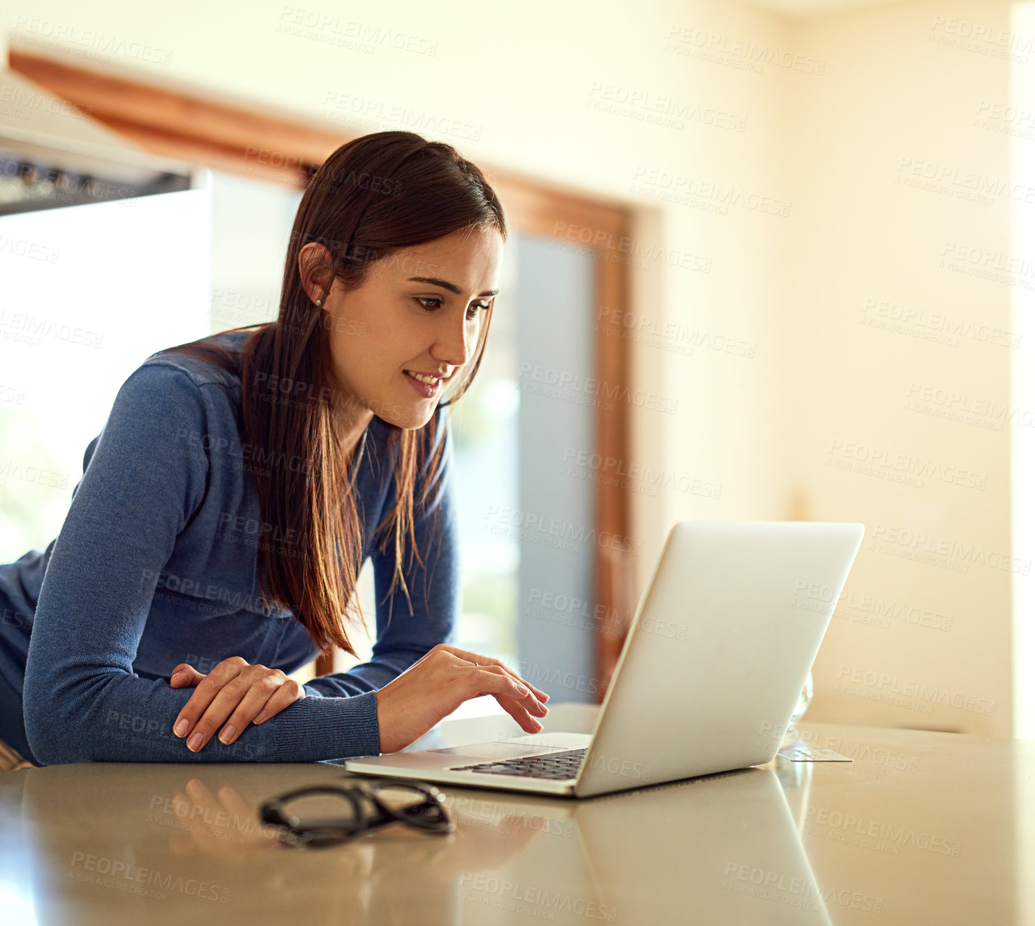 Buy stock photo Shot of a happy young woman using her laptop while standing in her kitchen