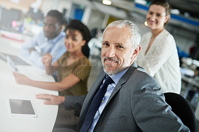 Buy stock photo Portrait of a mature man sitting at a table in an office with colleagues in the background