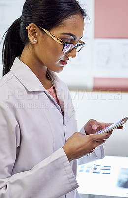 Buy stock photo Cropped shot of a young female dentist texting on her cellphone in her office
