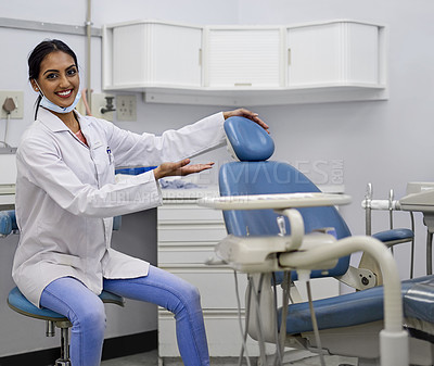 Buy stock photo Portrait of a young female dentist gesturing to sit in the dental chair in her office