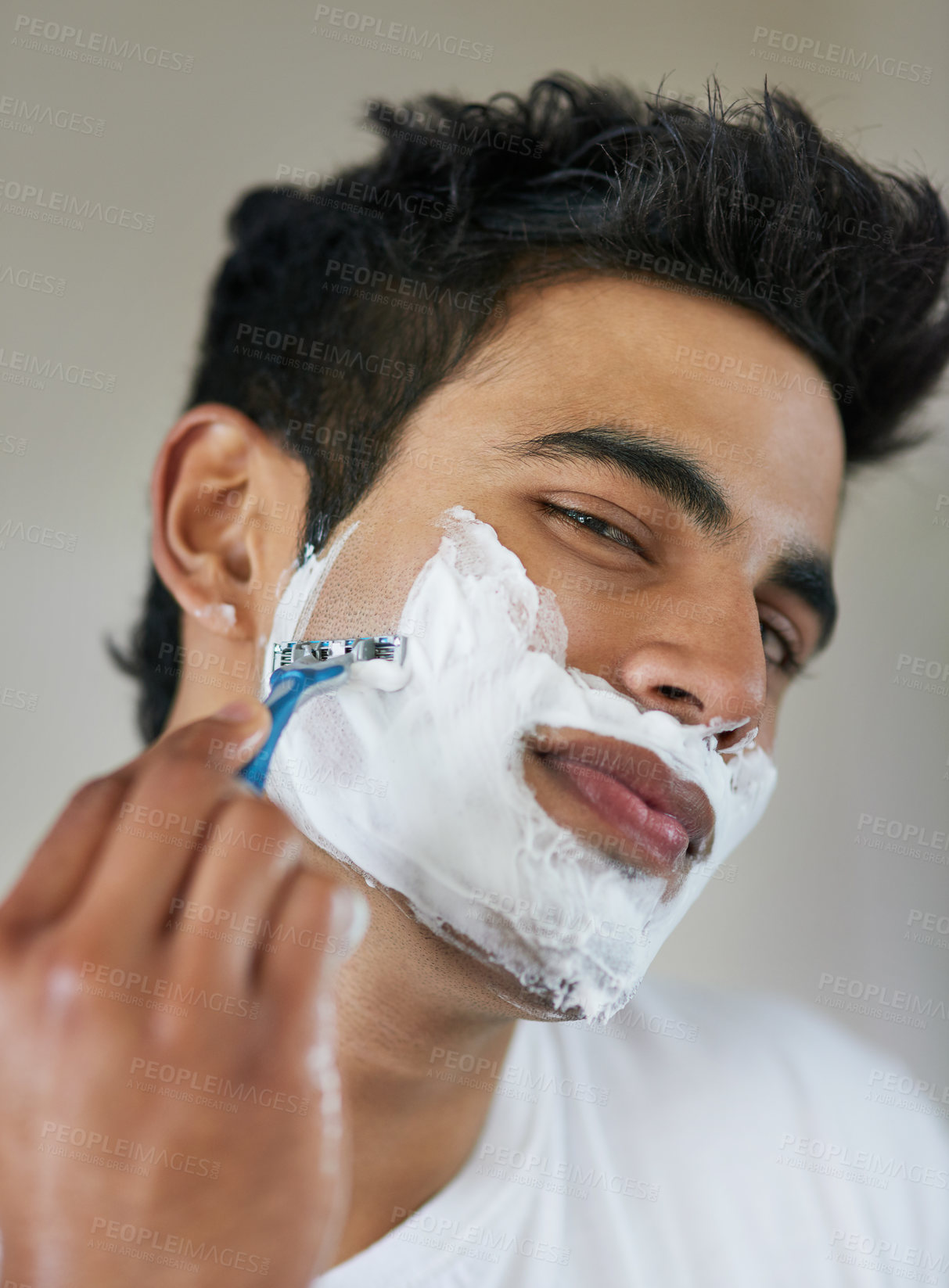 Buy stock photo Shot of a handsome young man shaving his facial hair in the bathroom