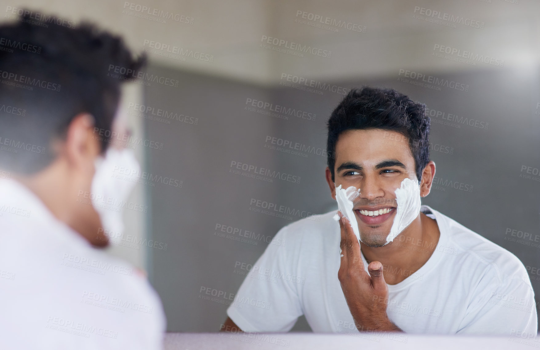 Buy stock photo Shot of a handsome young man shaving his facial hair in the bathroom