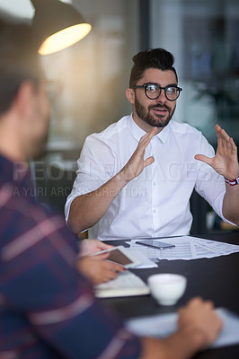 Buy stock photo Shot of a young professional leading his team through an idea while sitting at a table in an office