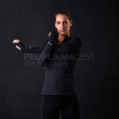 Buy stock photo Studio portrait of a young woman in gym clothes stretching her arms against a dark background