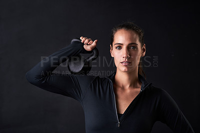 Buy stock photo Studio portrait of a young woman in gym clothes holding a kettlebell against a dark background