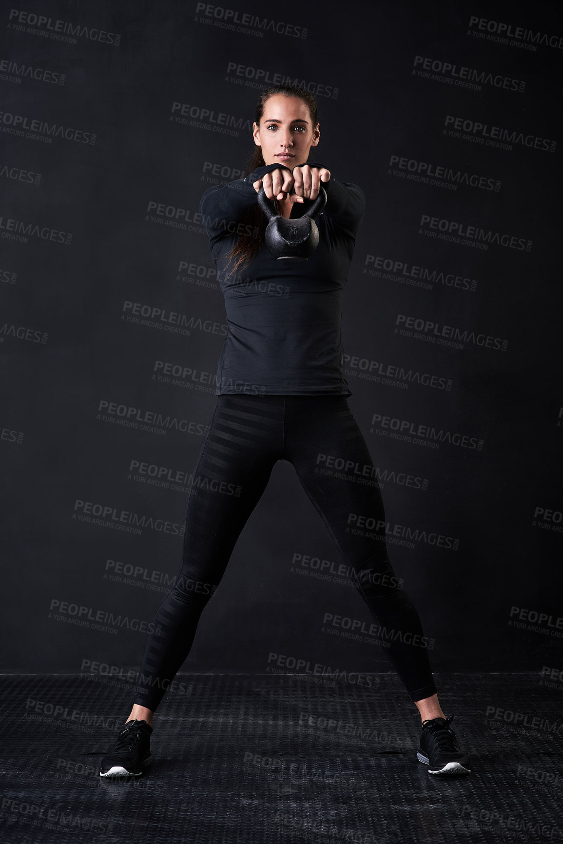 Buy stock photo Studio portrait of a young woman in gym clothes working out with a kettlebell against a dark background