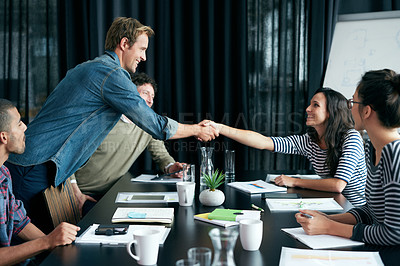 Buy stock photo Shot of two colleagues shaking hands in a boardroom while coworkers look on