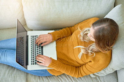 Buy stock photo High angle shot of a young woman using her laptop while sitting on the sofa at home