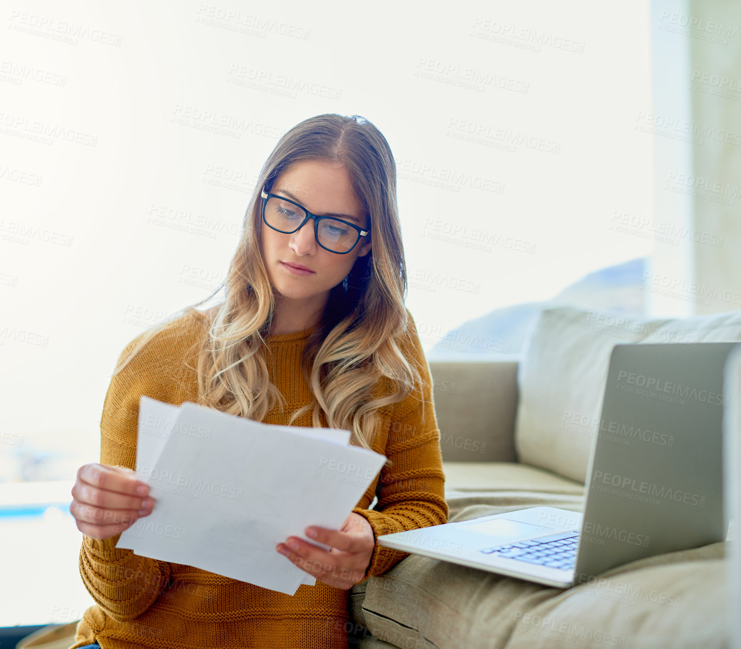 Buy stock photo Shot of an attractive young woman reading paperwork while working at home