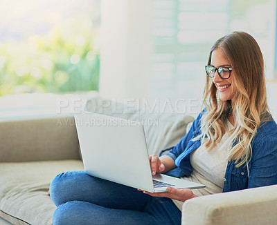 Buy stock photo Shot of an attractive young woman using her laptop while sitting on the sofa at home
