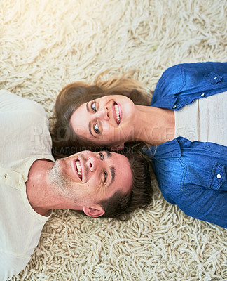 Buy stock photo High angle shot of an affectionate young couple lying on their living room floor
