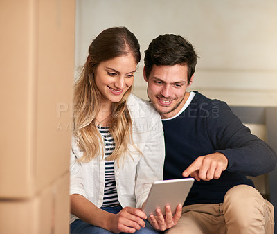 Buy stock photo Shot of a happy young couple taking a break with their tablet while moving into their new home