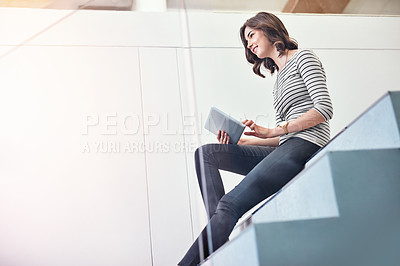 Buy stock photo Shot of a young designer using her tablet while sitting on the stairs in the office