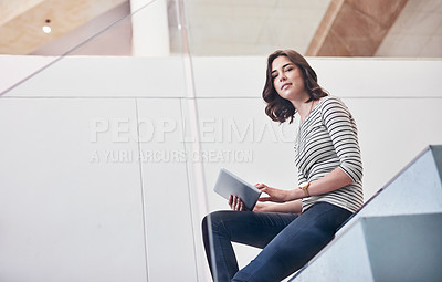Buy stock photo Portrait of a young designer using her tablet while sitting on the stairs in the office