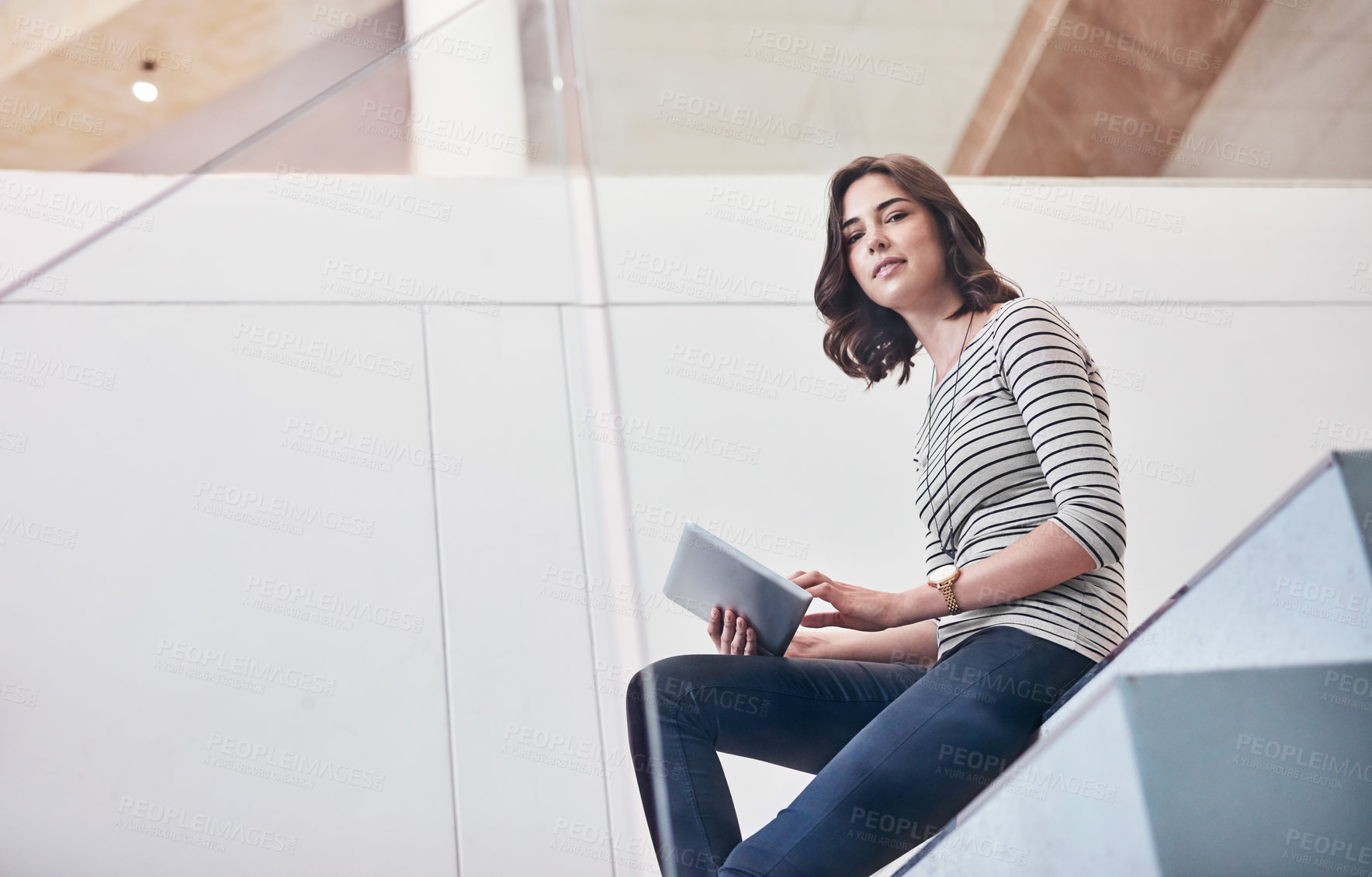 Buy stock photo Portrait of a young designer using her tablet while sitting on the stairs in the office