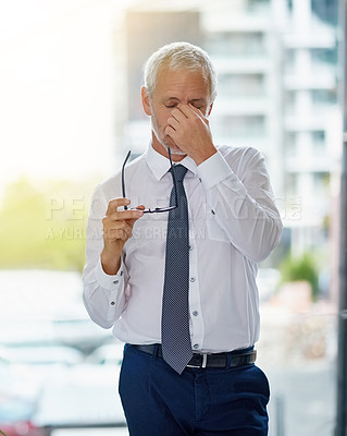Buy stock photo Shot of a mature businessman looking exhausted while standing in an office