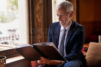 Buy stock photo Shot of a well-dressed mature man reading a menu in a cafe after work