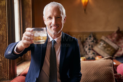 Buy stock photo Portrait of a well-dressed mature man making a toast with a glass of whiskey in a bar after work