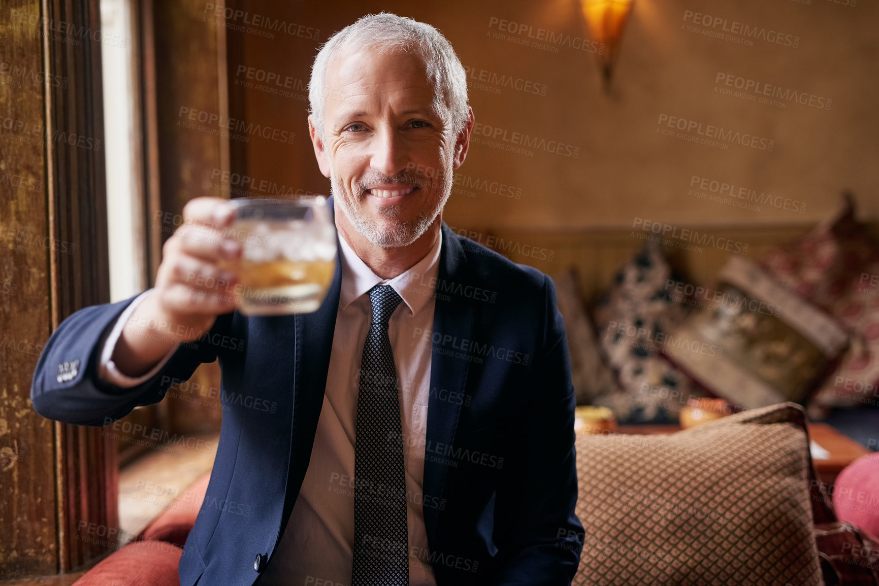 Buy stock photo Portrait of a well-dressed mature man making a toast with a glass of whiskey in a bar after work