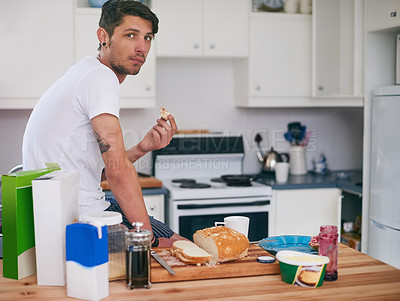 Buy stock photo Portrait of a handsome young man standing in his kitchen making a sandwich