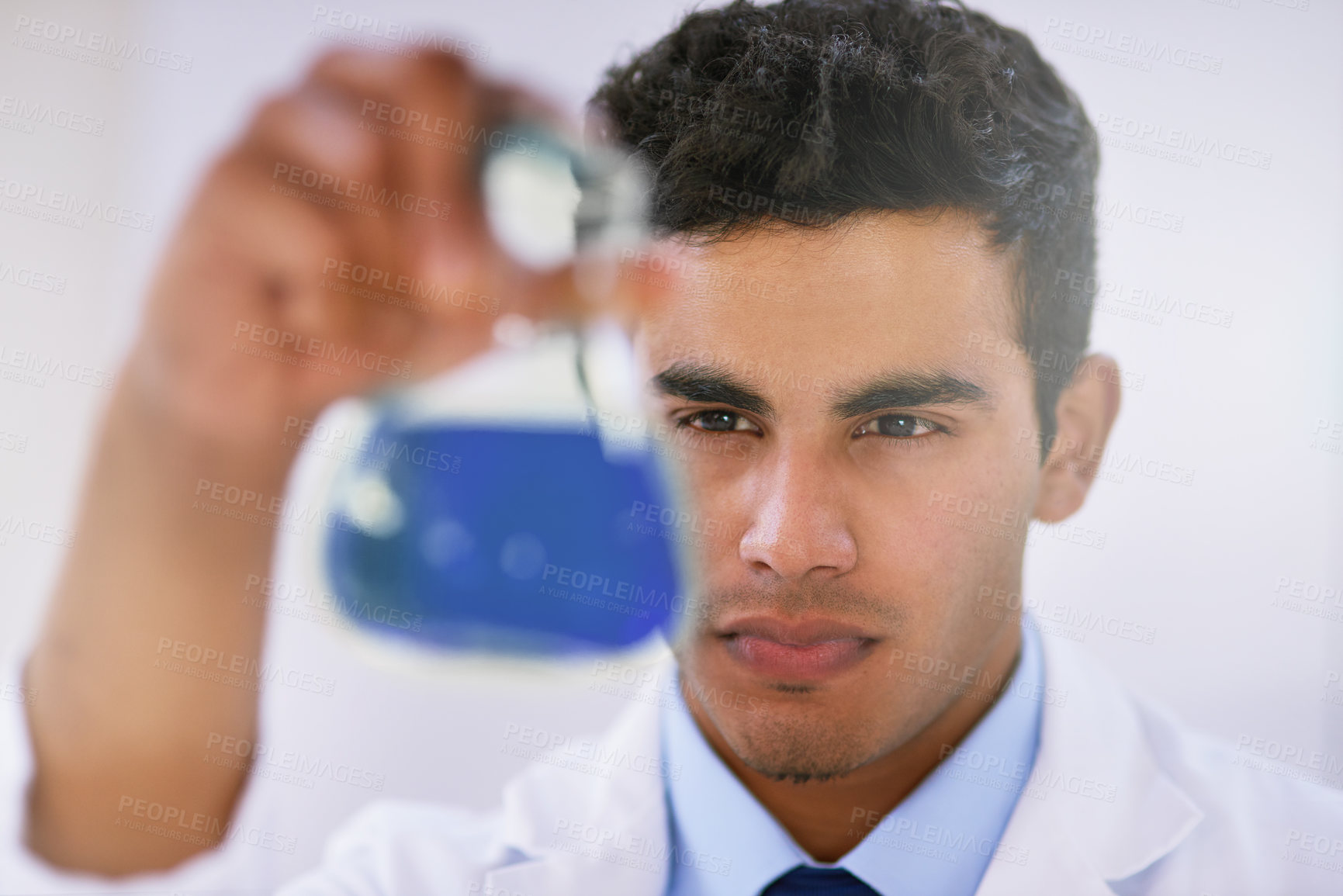 Buy stock photo Shot of a lab technician examining a beaker of blue liquid while standing in a lab