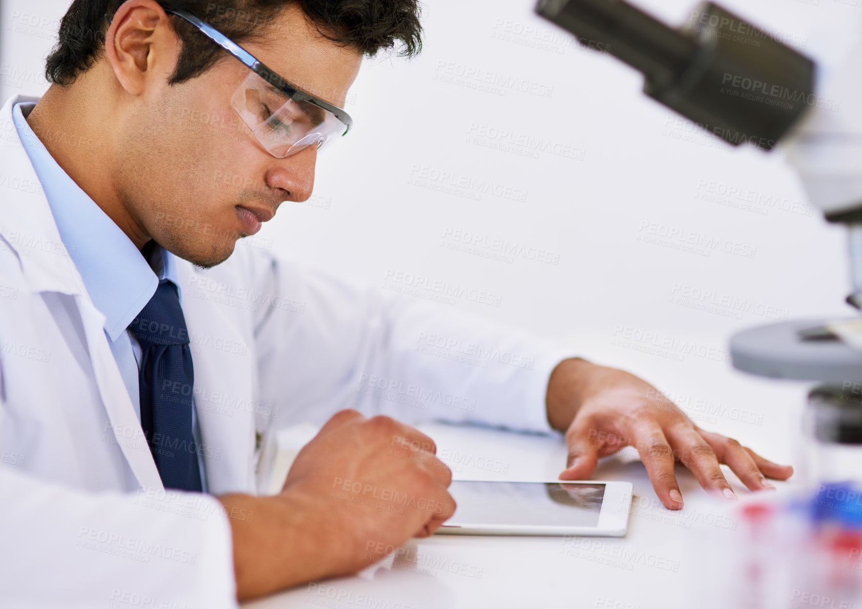 Buy stock photo Scientist, man and microscope in laboratory with tablet, safety goggles and study with app for bacteria evolution. Person, technician and thinking with tools, analysis and DNA research on touchscreen