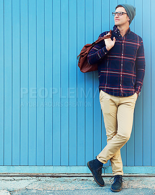 Buy stock photo Shot of a handsome young man leaning against a blue wall