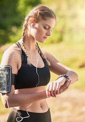 Buy stock photo Shot of an attractive young woman listening to music while timing her run