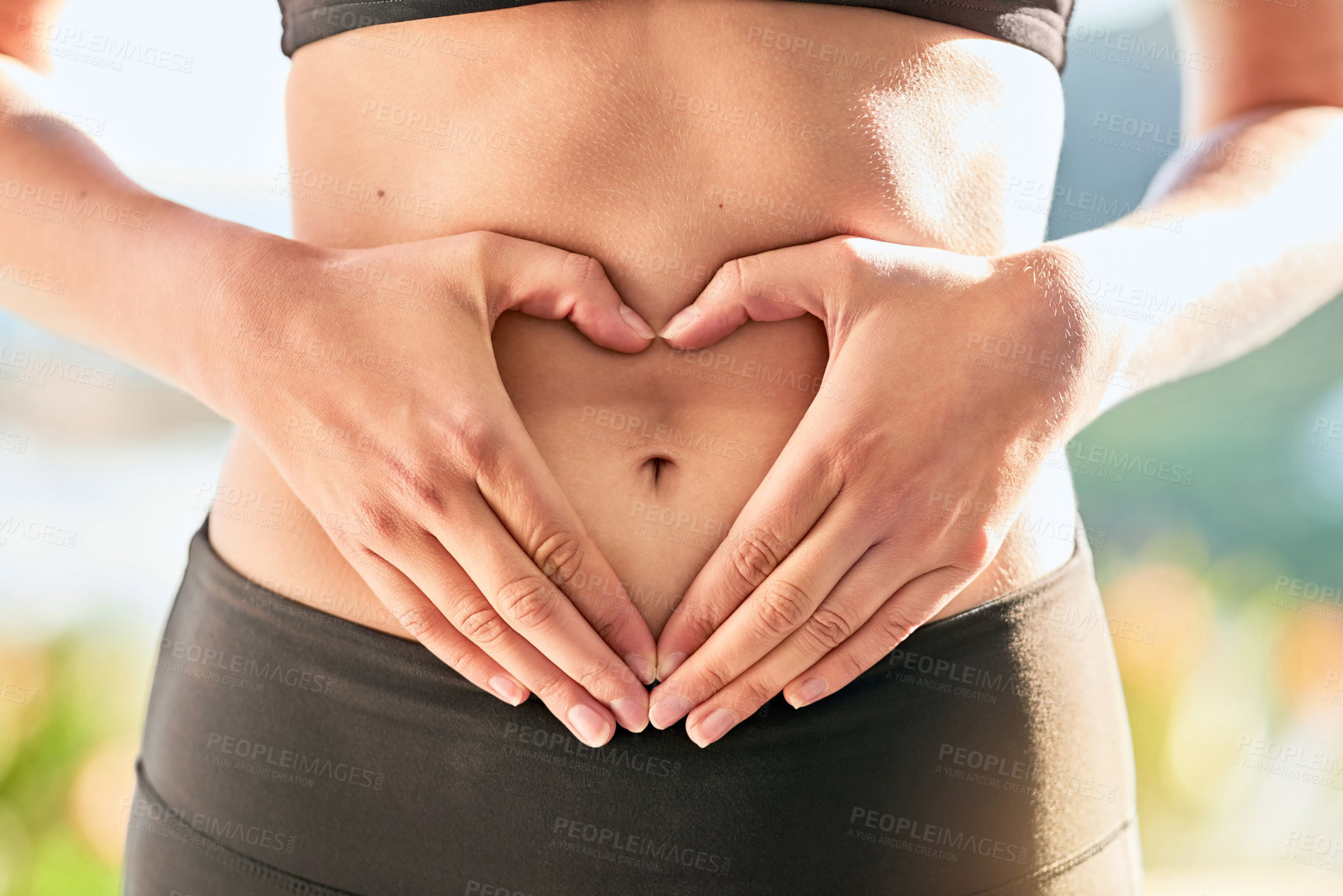 Buy stock photo Shot of an unrecognizable young woman making a heart shape with her hands around her belly button