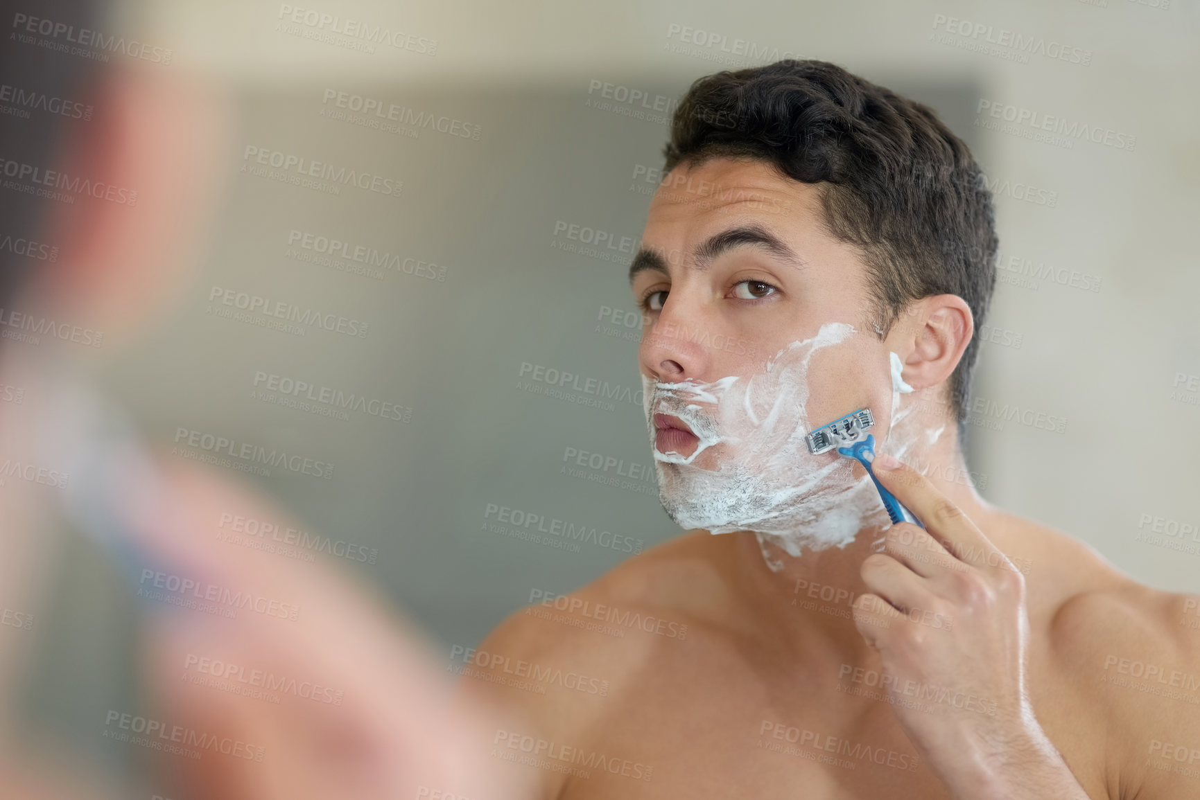 Buy stock photo Shot of a handsome young man shaving his facial hair in the bathroom