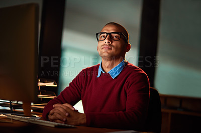 Buy stock photo Shot of a handsome young man looking thoughtful while working late in his office