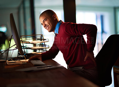 Buy stock photo Shot of a young man holding his back in pain while working late in the office