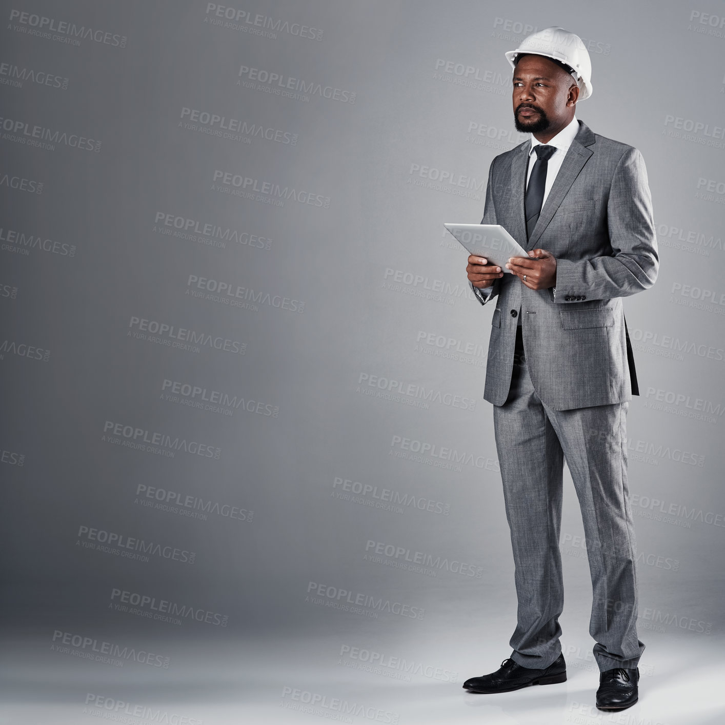 Buy stock photo Architect, man and tablet in studio with thinking, suit and helmet with mockup space by gray background. African person, insight and touchscreen with application, review and floor plan for project