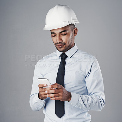 Buy stock photo Shot of a well-dressed civil engineer using his cellphone while standing in the studio