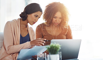 Buy stock photo Shot of two young coworkers going through paperwork and using a laptop together