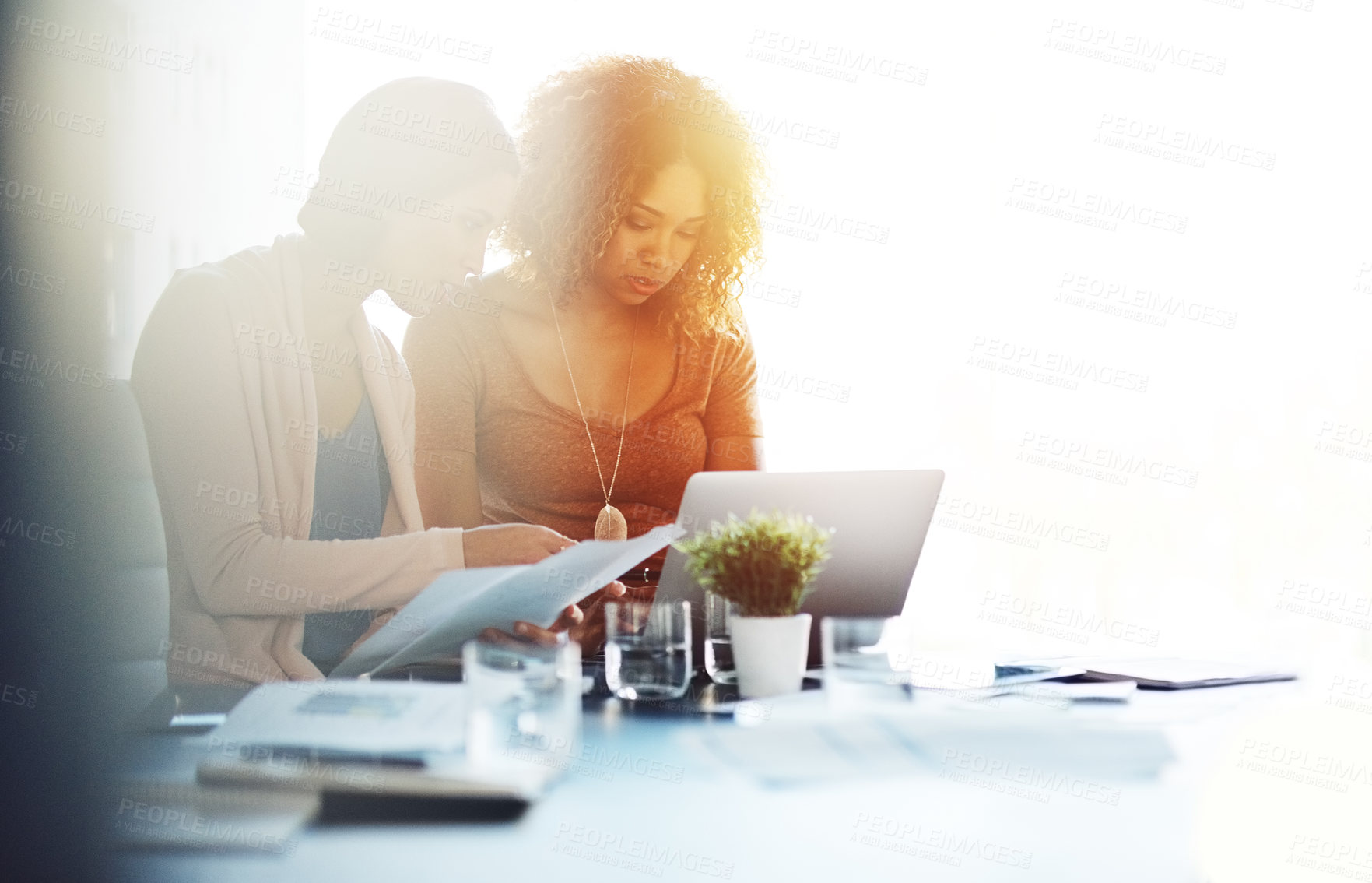 Buy stock photo Shot of two young coworkers going through paperwork and using a laptop together