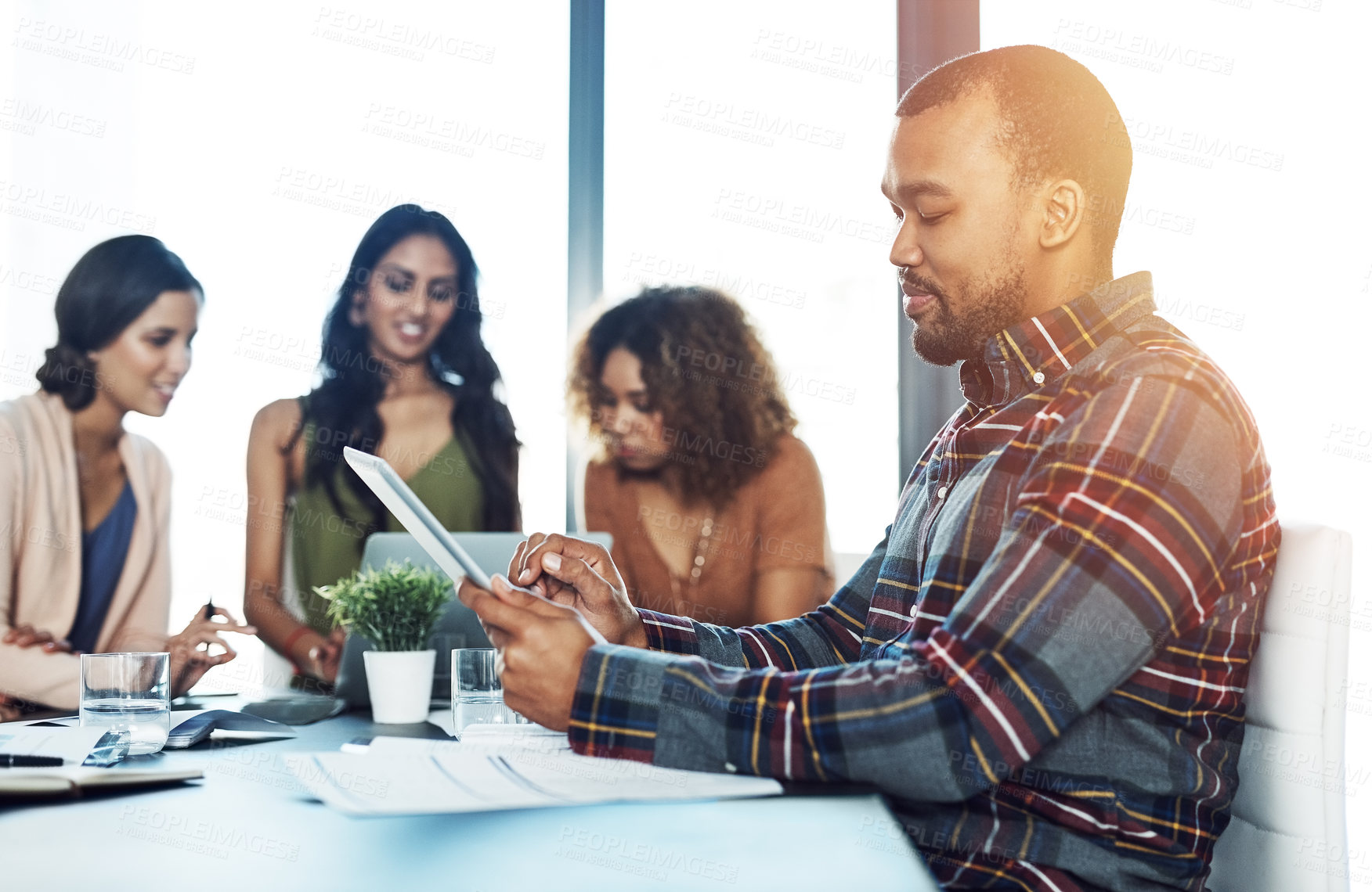 Buy stock photo Shot of a young man using a digital tablet during a meeting with his colleagues in the background