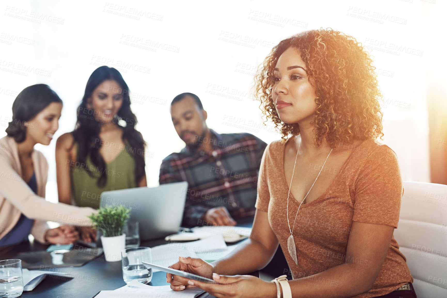 Buy stock photo Shot of a young woman using a digital tablet during a meeting with her colleagues in the background