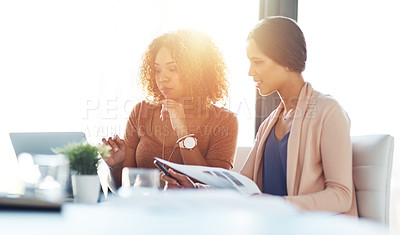 Buy stock photo Shot of two young coworkers going through paperwork and using a laptop together