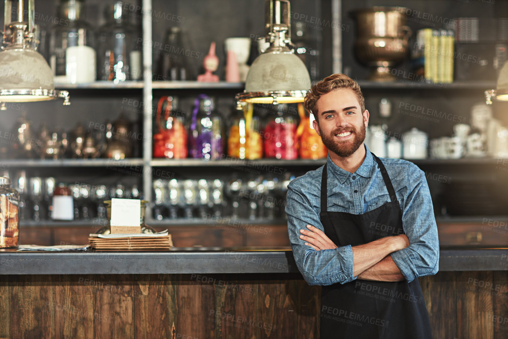 Buy stock photo Happy, crossed arms and portrait of male barista standing by the counter in his startup cafeteria. Smile, success and young man small business owner with confidence in coffee shop or restaurant.