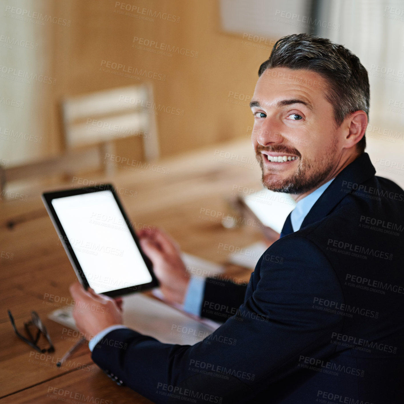 Buy stock photo Portrait of a smiling executive using a digital tablet while sitting alone at a table in an office