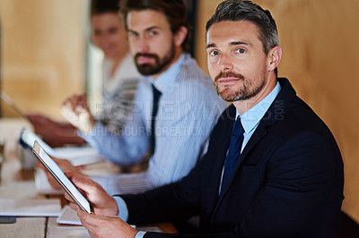 Buy stock photo Portrait of a businessman with a digital tablet sitting at a table with colleagues in the background