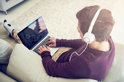 Buy stock photo High angle shot of a young man listening to music on his laptop while sitting on his sofa at home